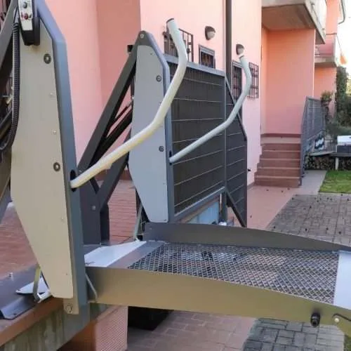 Outdoor wheelchair platform lift raised to landing height at a home entrance door Outdoor wheelchair platform lift raised to landing height at a home entrance door