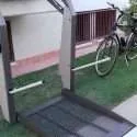 Open platform of a wheelchair lift with non-slip mesh surface and fold-up access ramp